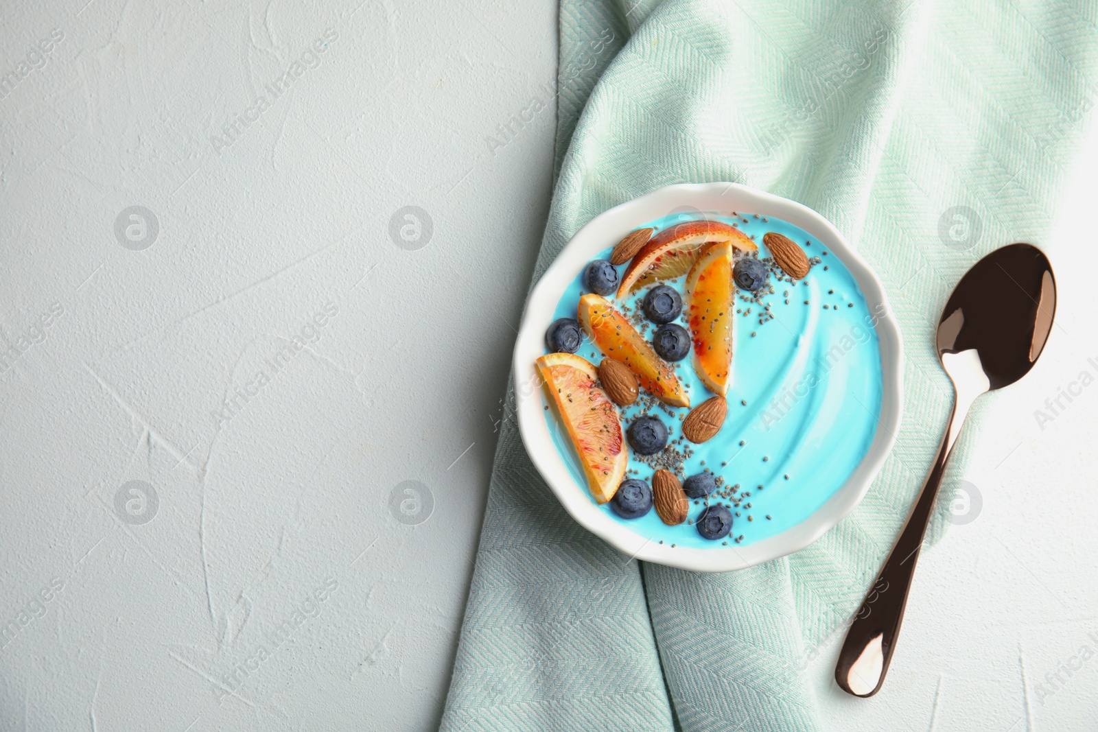 Photo of Bowl of spirulina smoothie, napkin and spoon on light background, top view with space for text