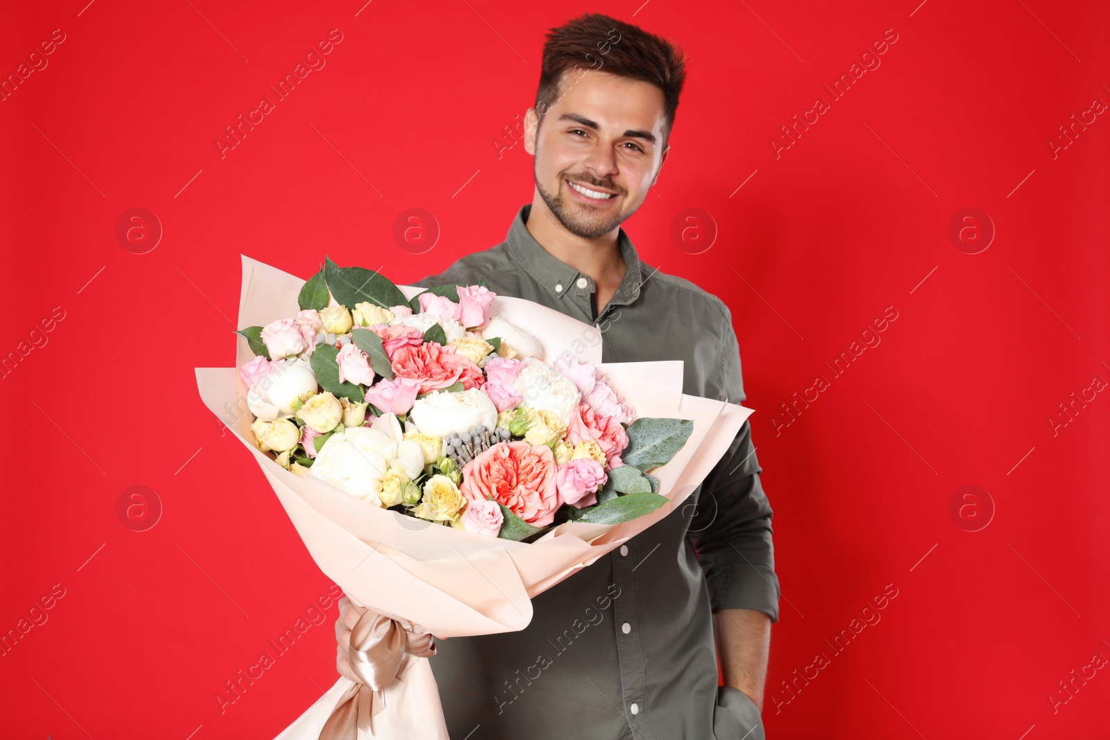 Photo of Young handsome man with beautiful flower bouquet on red background