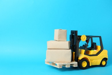 Toy forklift with wooden pallet and boxes on light blue background, space for text