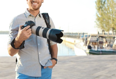 Photo of Young male photographer holding professional camera at pier. Space for text