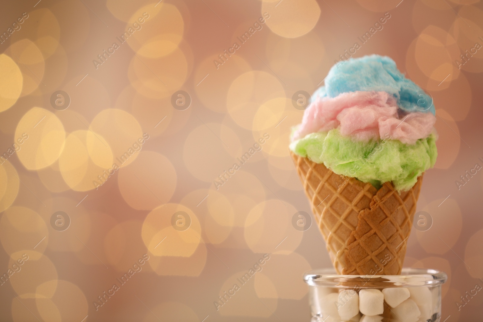 Photo of Sweet cotton candy in waffle cone against blurred lights, closeup. Space for text