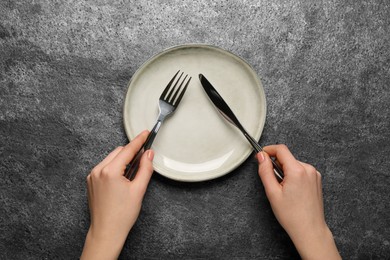 Photo of Woman with empty plate and cutlery at grey table, top view