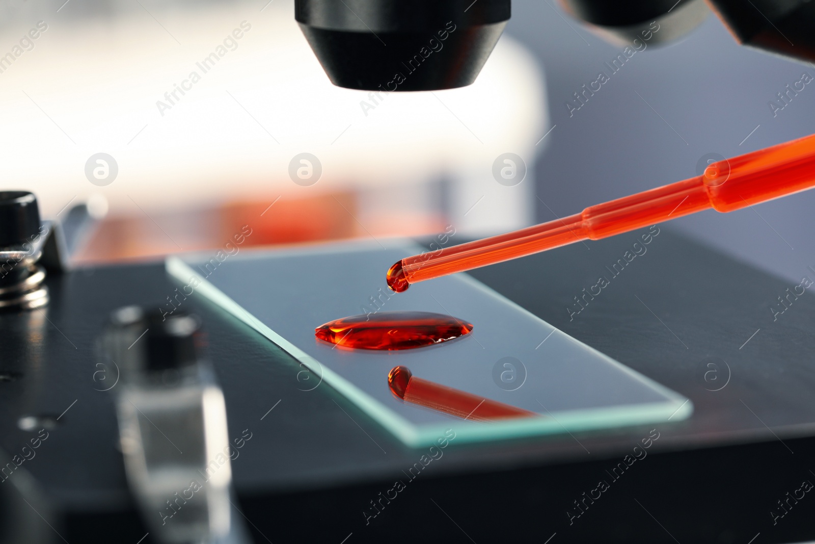 Photo of Dripping sample of red liquid onto slide under microscope in laboratory, closeup