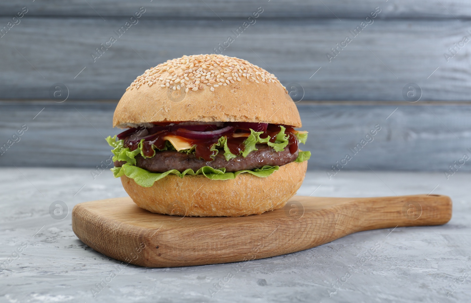 Photo of Delicious cheeseburger with ketchup and patty on grey textured table