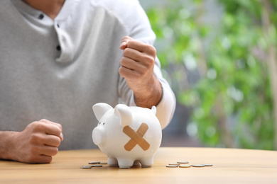 Photo of Man and piggy bank with medical patches at table. Space for text