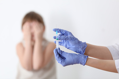 Photo of Doctor holding syringe with chickenpox vaccine and scared child on background, closeup. Varicella virus prevention