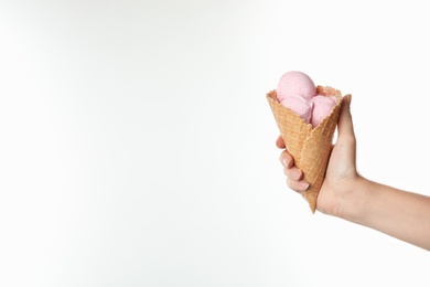 Woman holding delicious ice cream in waffle cone on white background, closeup