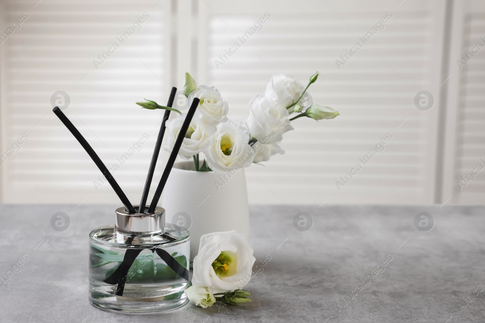 Photo of Reed diffuser and vase with eustoma flowers on gray marble table, space for text