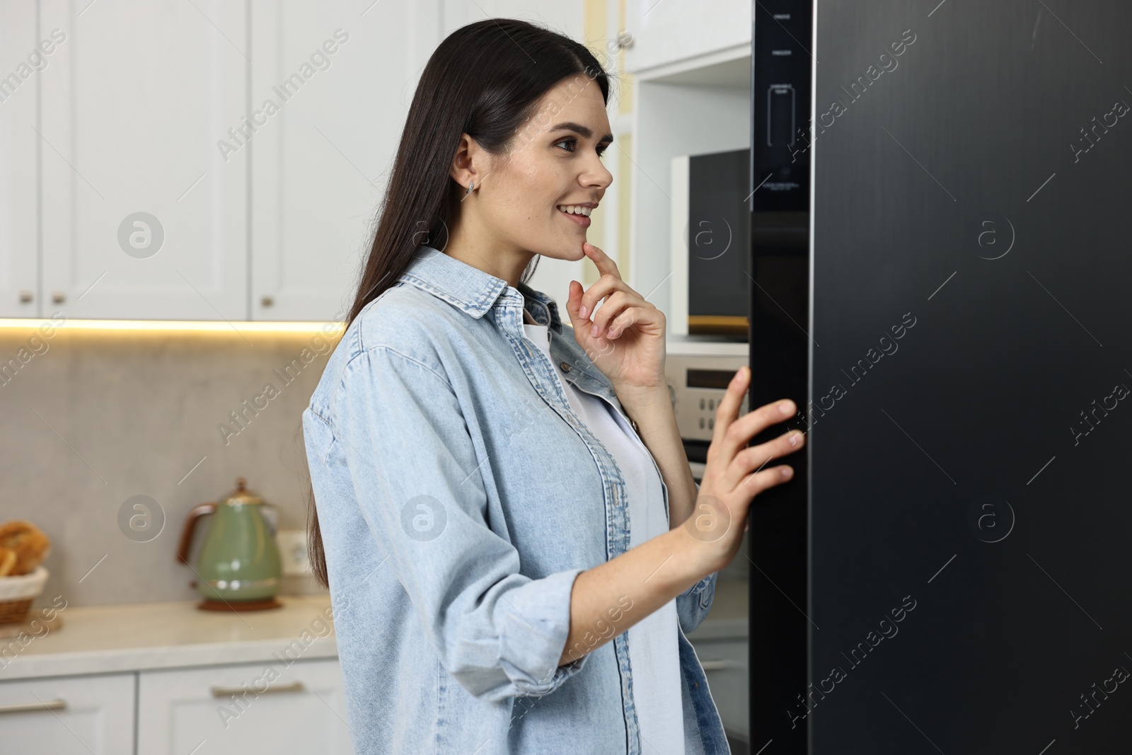 Photo of Thoughtful young woman near modern refrigerator in kitchen