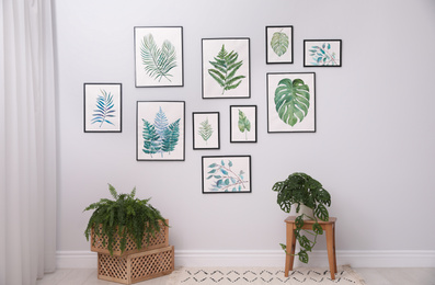 Photo of Beautiful paintings of tropical leaves on white wall in living room interior