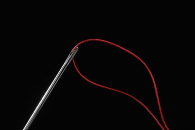 Sewing needle with red thread on black background, closeup