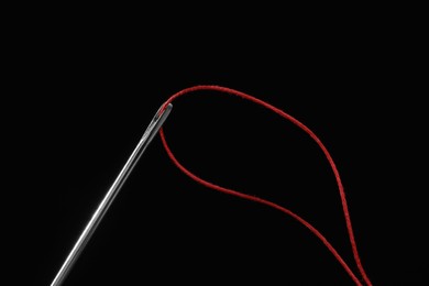 Photo of Sewing needle with red thread on black background, closeup