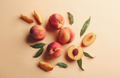 Photo of Fresh ripe peaches and green leaves on beige background, flat lay