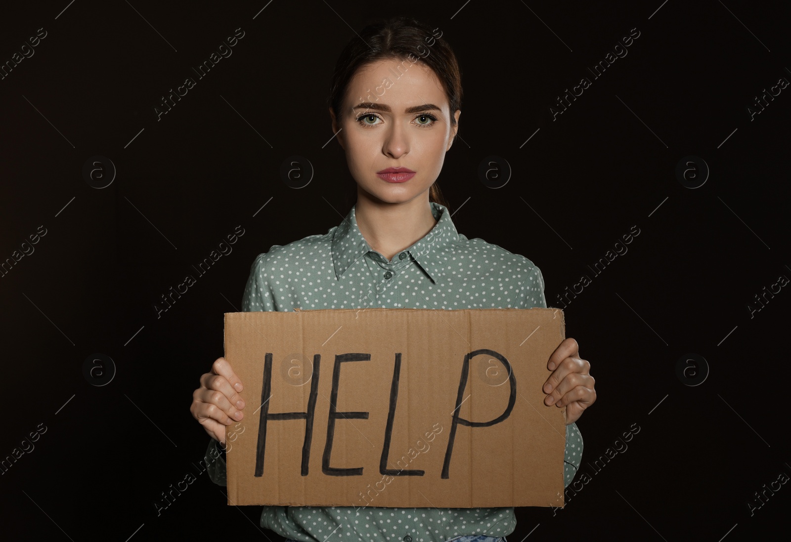 Photo of Unhappy young woman with HELP sign on dark background