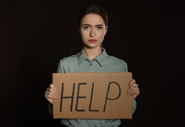 Unhappy young woman with HELP sign on dark background