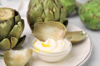 Delicious cooked artichokes with tasty sauce served on table, closeup