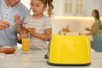 Photo of Father and daughter having breakfast at table in kitchen, focus on toaster