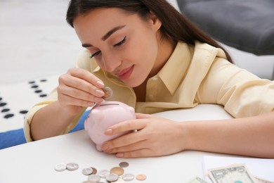 Photo of Woman putting coin into piggy bank indoors. Money savings