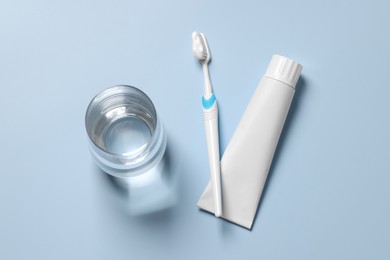 Plastic toothbrush with paste and glass of water on light background, flat lay