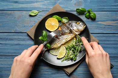 Photo of Woman eating delicious roasted fish at blue wooden table, top view