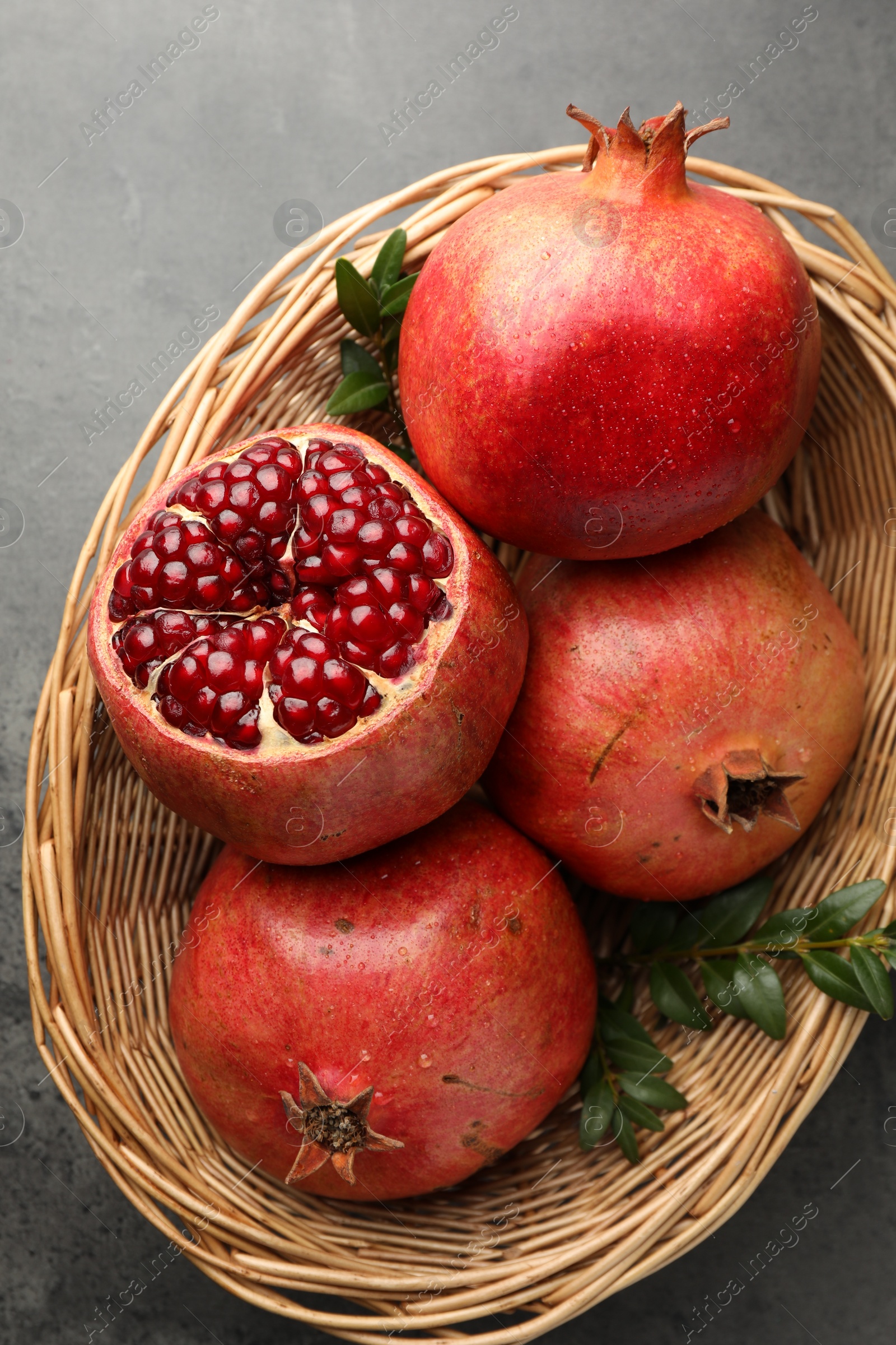 Photo of Fresh pomegranates and green leaves in wicker basket on grey table, top view