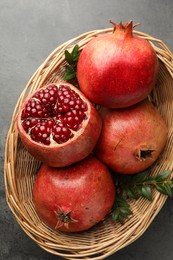 Photo of Fresh pomegranates and green leaves in wicker basket on grey table, top view