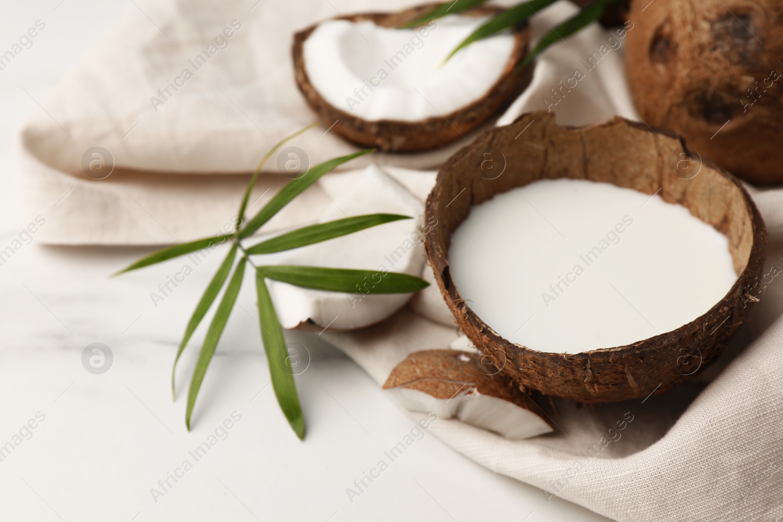 Photo of Delicious vegan milk in coconut, leaf and pieces of ripe fruit on white marble table, closeup