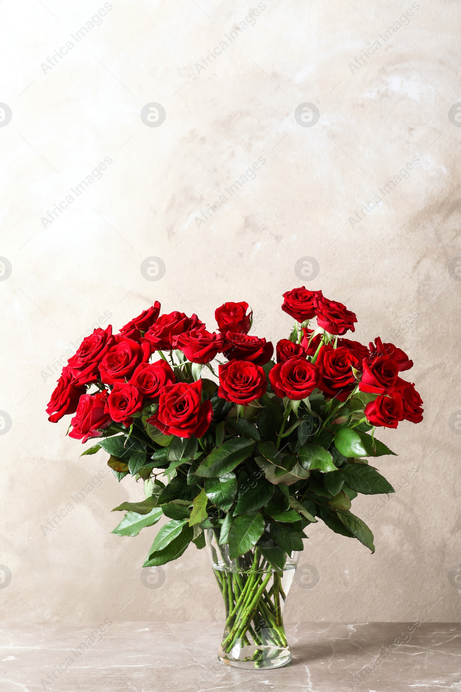 Photo of Vase with beautiful red roses on table against color background