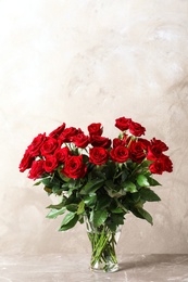 Vase with beautiful red roses on table against color background