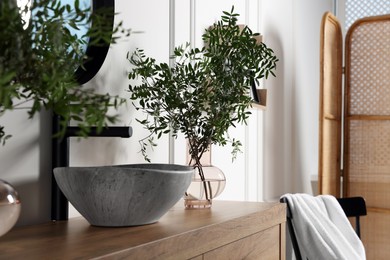 Photo of Eucalyptus branches near vessel sink on bathroom vanity. Interior design