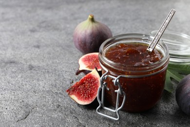 Photo of Jar of tasty sweet jam and fresh figs on grey table, closeup. Space for text