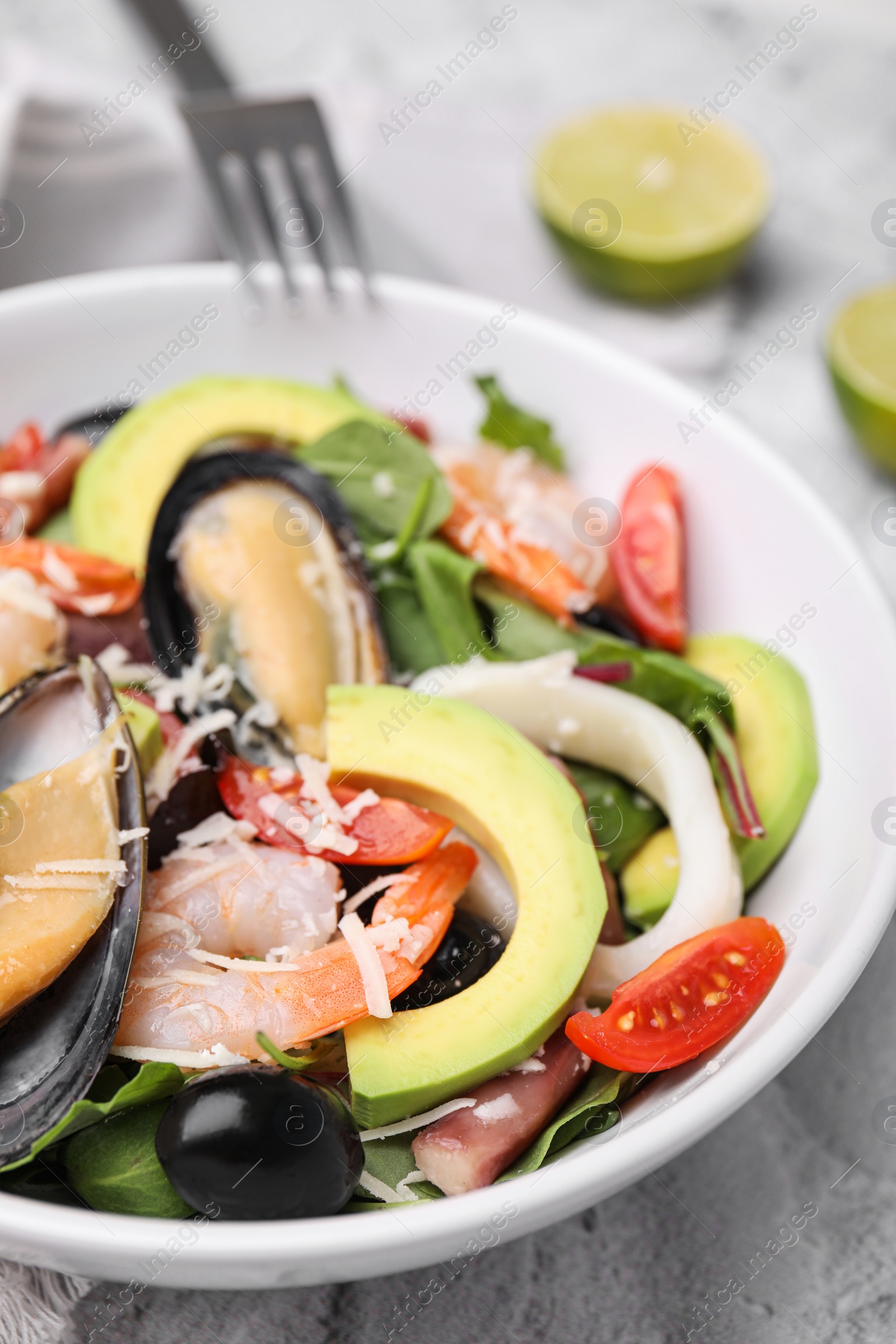 Photo of Bowl of delicious salad with seafood on white textured table, closeup