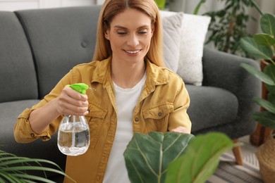 Photo of Woman spraying beautiful houseplants with water at home