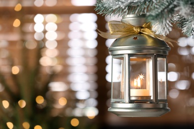 Beautiful Christmas lantern with burning candle hanging on fir tree branch in room. Space for text