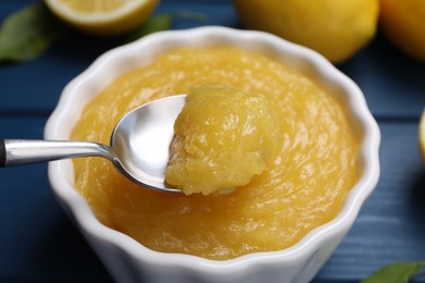 Taking delicious lemon curd from bowl at blue table, closeup