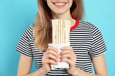 Young woman with delicious shawarma on turquoise background, closeup