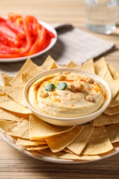Photo of Delicious creamy hummus served with chips on wooden table