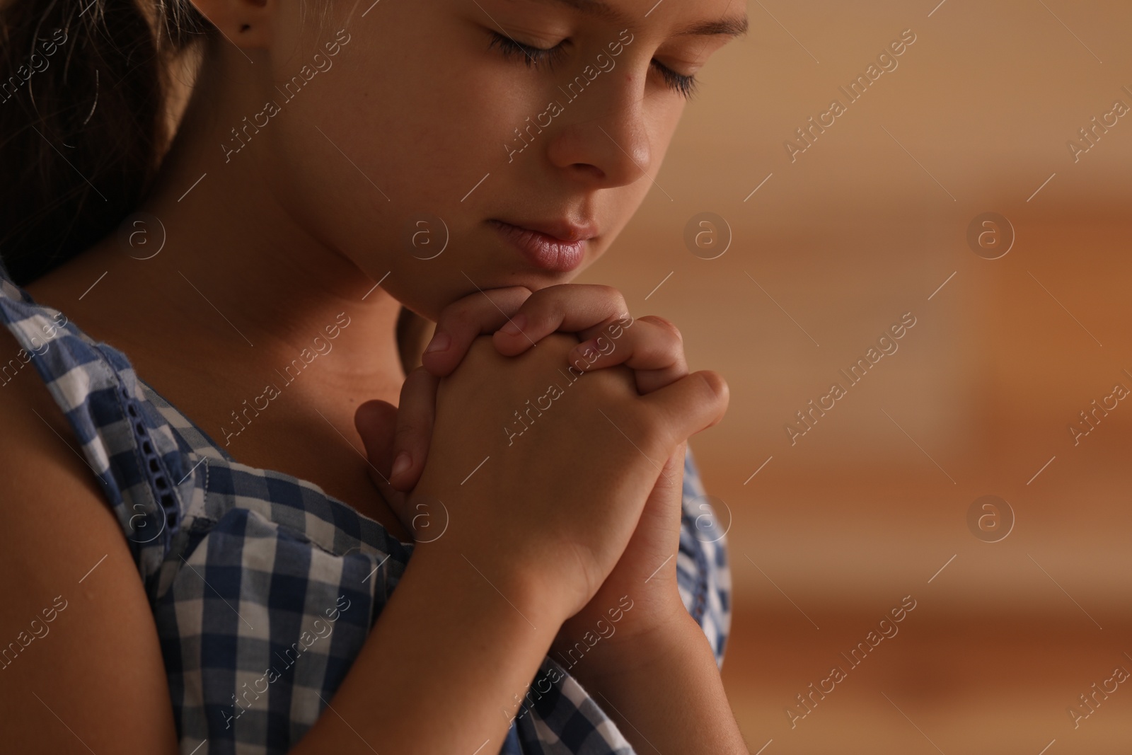 Photo of Cute little girl with hands clasped together praying on blurred background, closeup