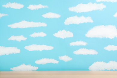 Wooden table near wall with painted blue sky. Idea for baby room interior