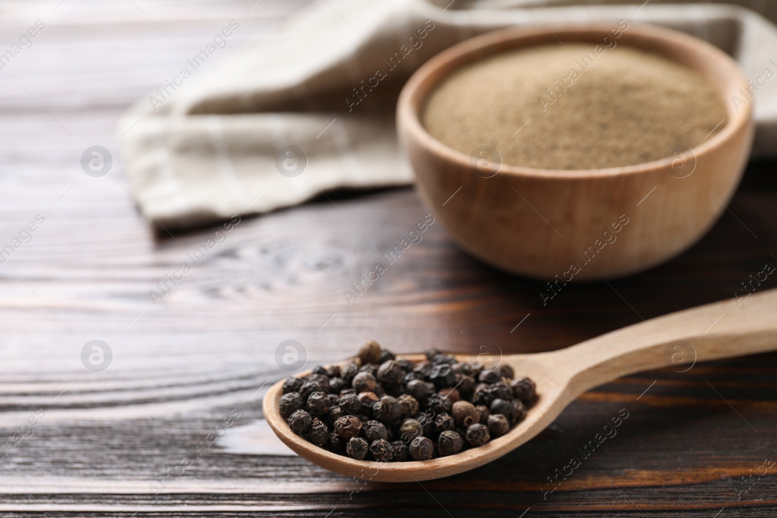 Photo of Peppercorns in spoon on wooden table, closeup