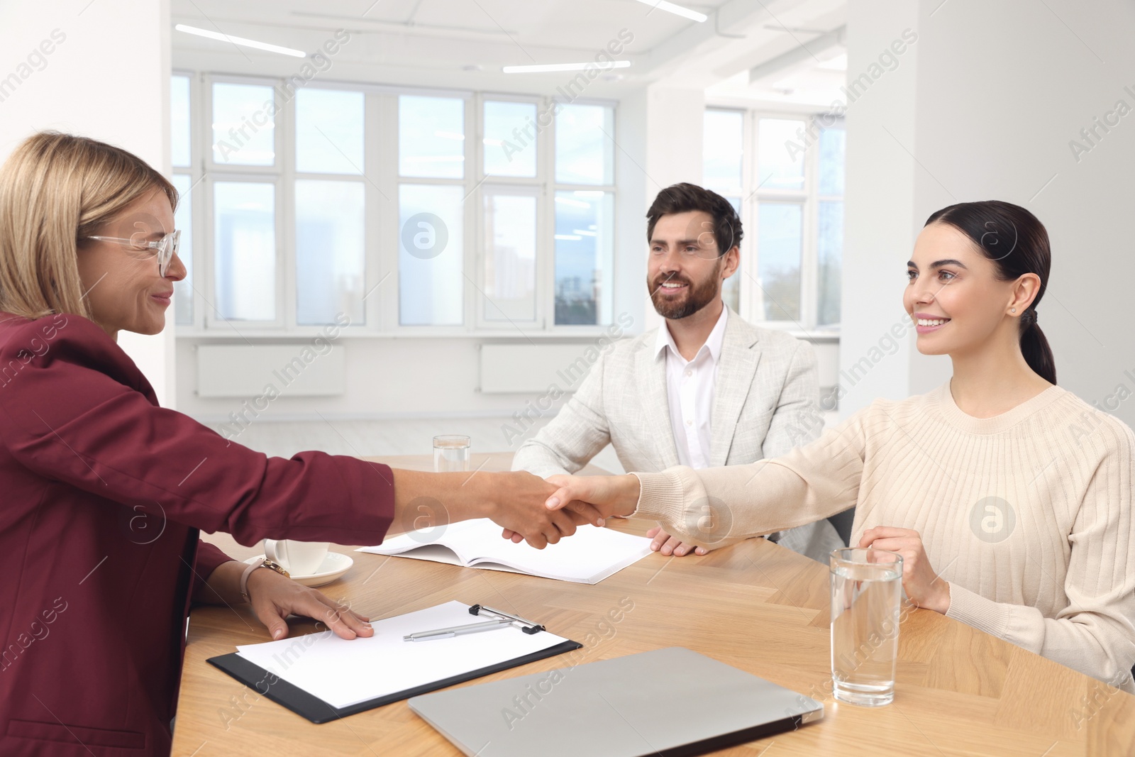 Photo of Real estate agent shaking hands with client at table in new apartment