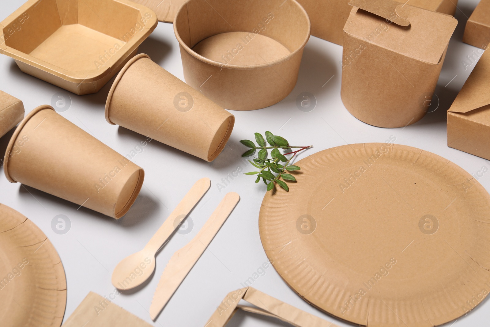 Photo of Eco friendly food packaging. Paper containers, tableware and green twigs on light grey background