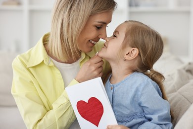 Photo of Little daughter congratulating her mom with greeting card at home. Happy Mother's Day