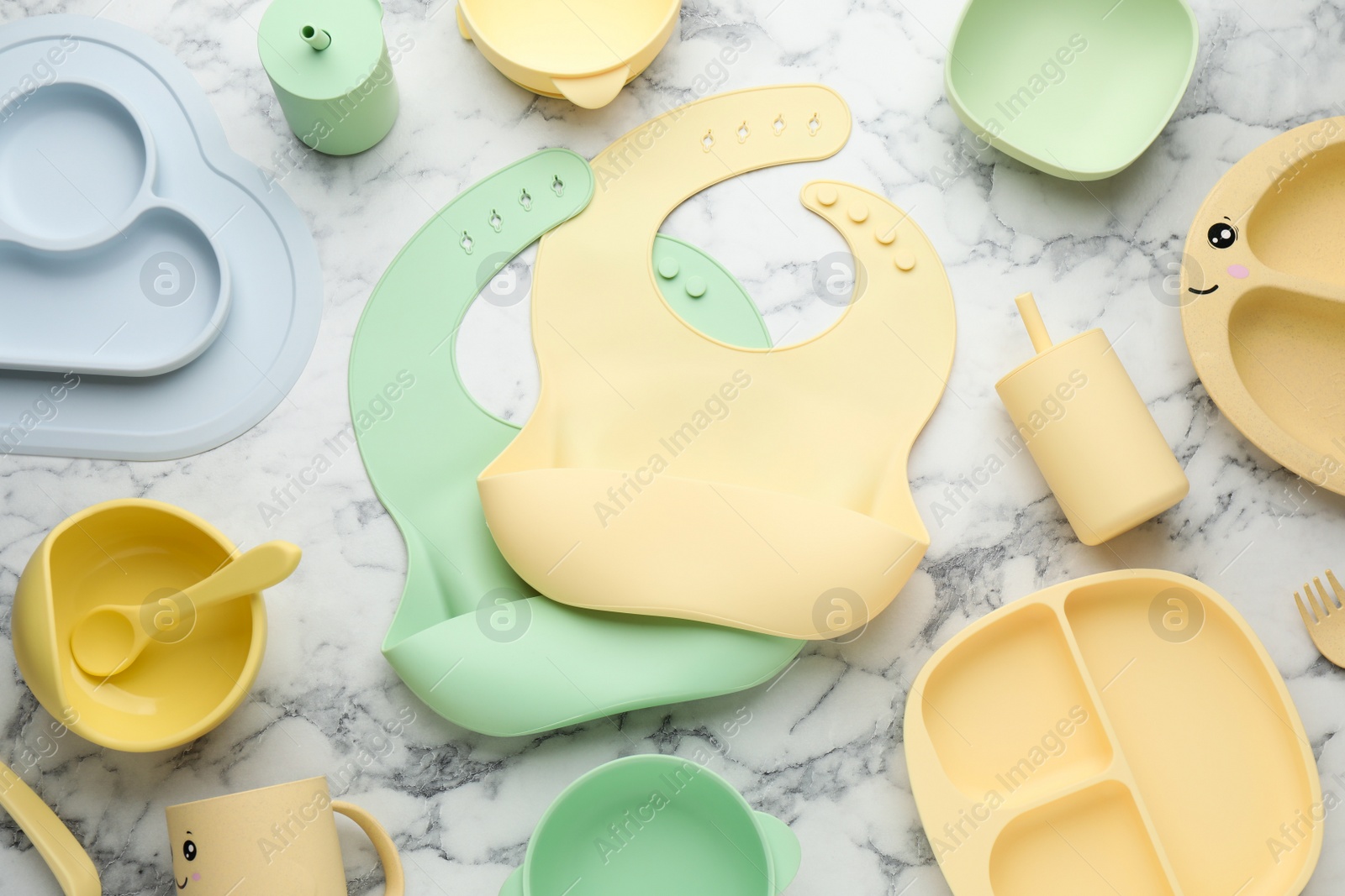 Photo of Flat lay composition with silicone baby bibs and plastic dishware on white marble background