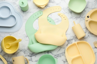 Photo of Flat lay composition with silicone baby bibs and plastic dishware on white marble background