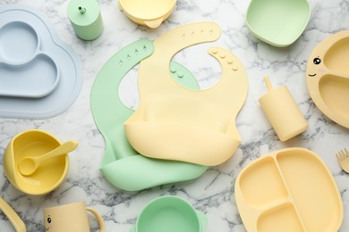 Flat lay composition with silicone baby bibs and plastic dishware on white marble background