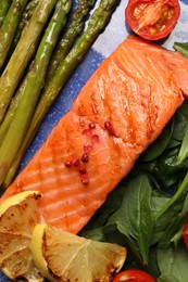 Photo of Tasty grilled salmon with tomatoes, asparagus, lemon and basil, top view