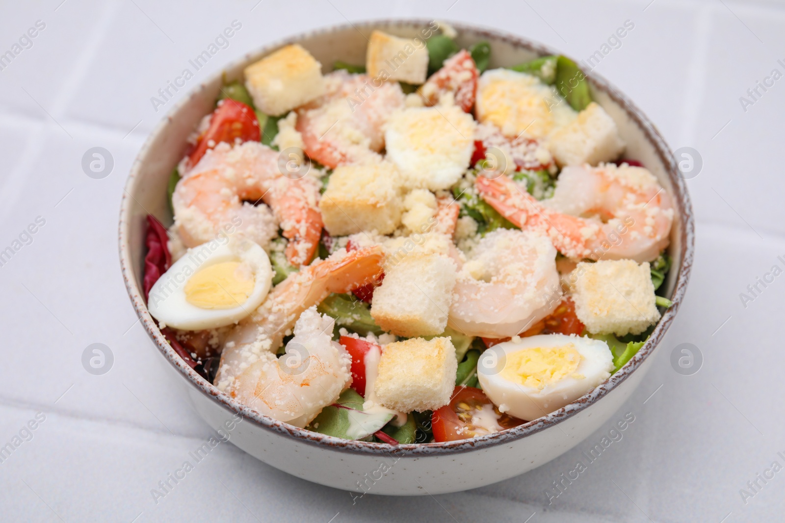 Photo of Delicious Caesar salad with shrimps on white tiled table, closeup