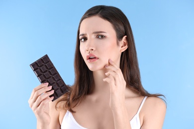 Photo of Teenage girl with acne problem holding chocolate bar against color background