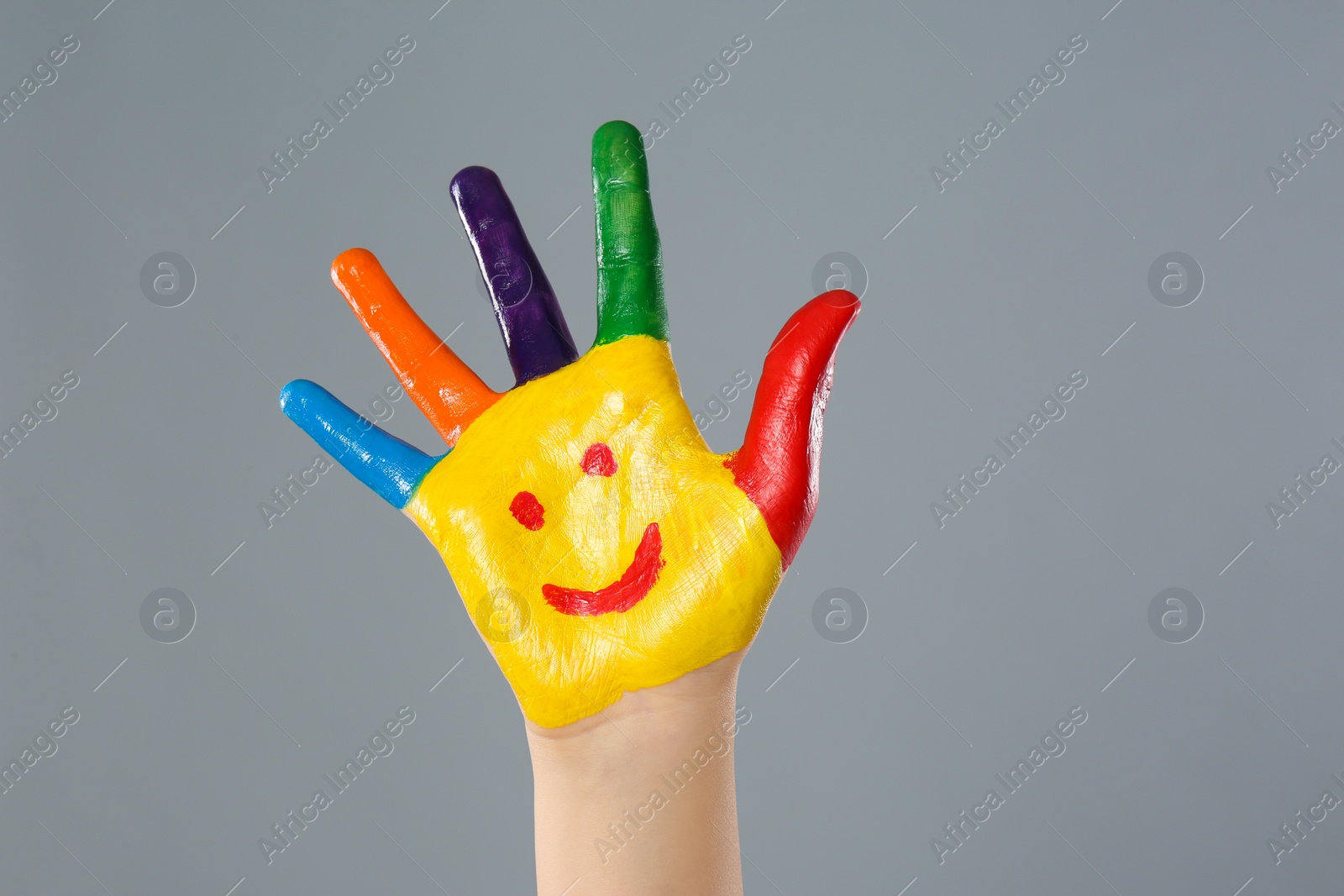 Photo of Kid with smiling face drawn on palm against grey background, closeup